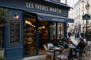 Parisian restaurant with a clean facade, clear signage, terrace tables, chalkboard menu, and a lively street setting in daylight.